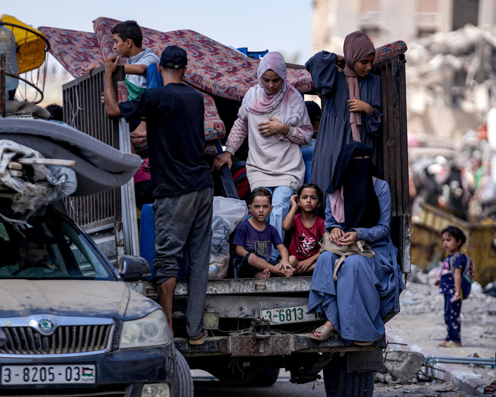 Women and children sit in the back of a damaged truck with belongings.