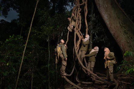 A team of female rangers climb on a large vine in the forest