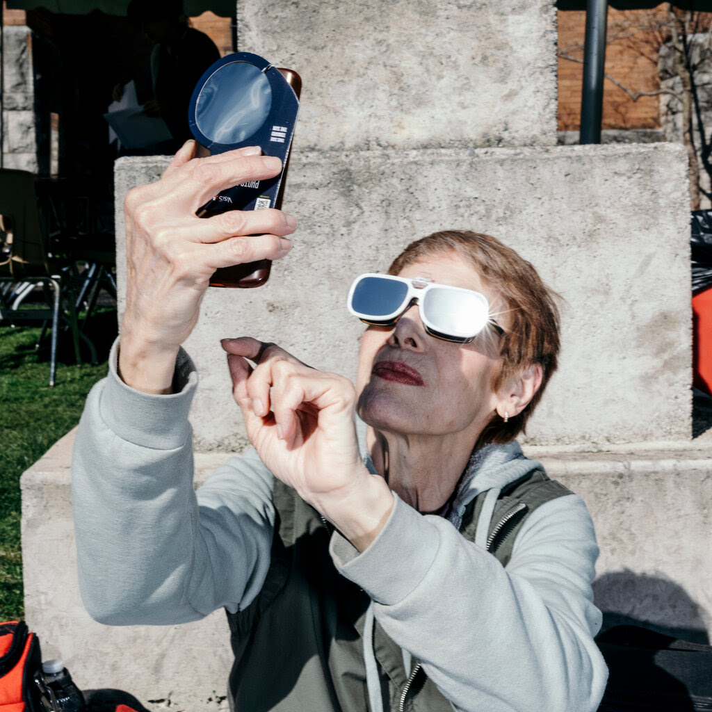 A woman looks at her phone which is held up at the sky. 