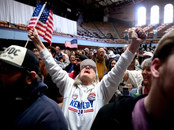  A woman wearing a Kennedy ‘24 sweatshirt throws her hands in the air at a rally.