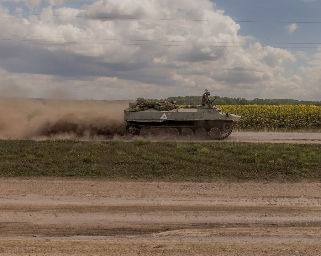 A military vehicle passing a field of sunflowers.