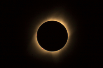 A total solar eclipse - the shadow of the moon blocks the surface of the sun, flares of light emanating from behind.