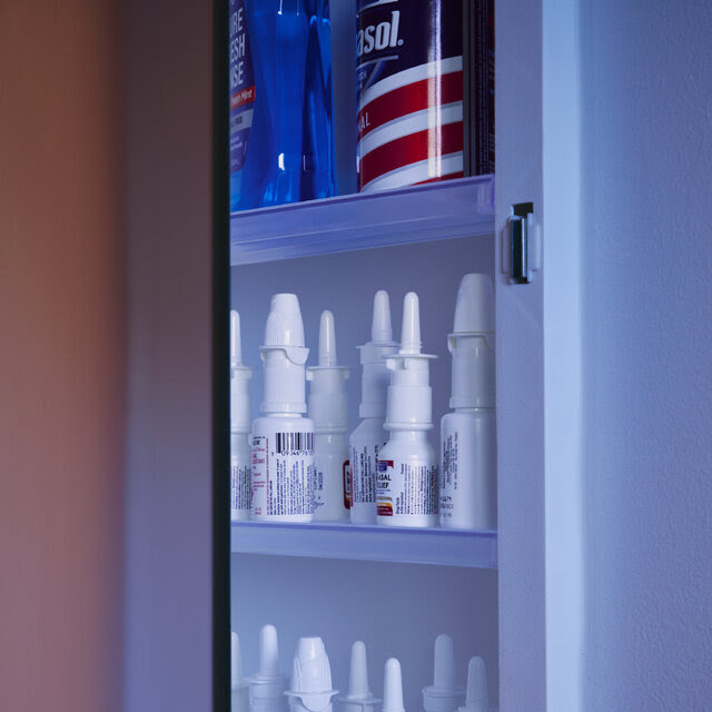 Several bottles of nasal spray line the shelves of a medicine cabinet.