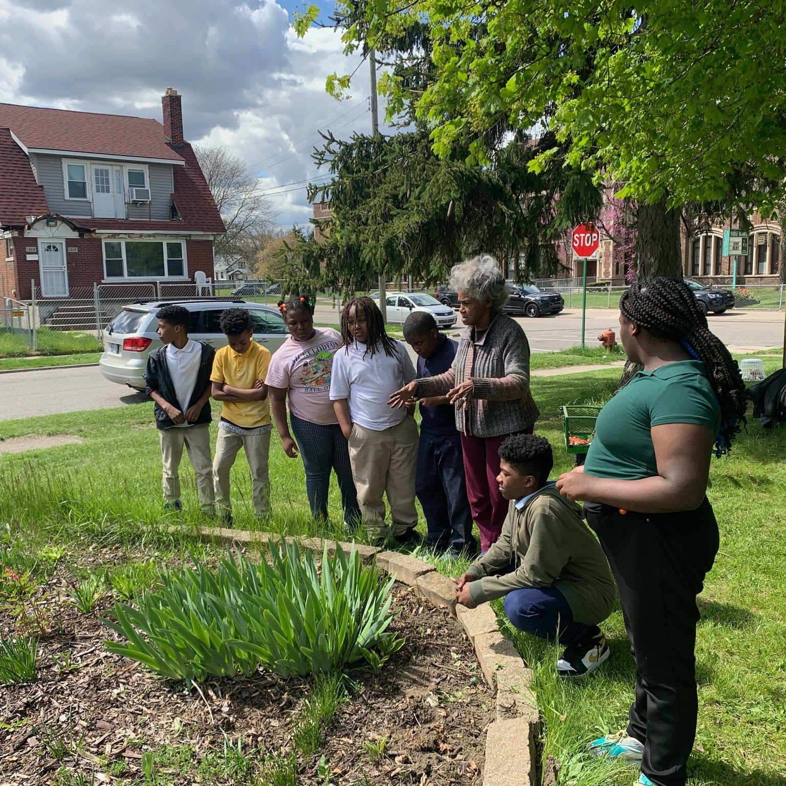 Young people gather around a garden in a neighborhood with an educator.