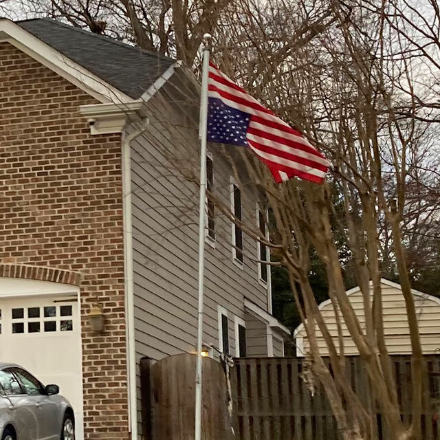 A brick house with an inverted American flag flying over a green suburban lawn. 