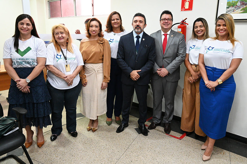 Analisando a imagem: os rostos podem estar desfocados para proteger a privacidade

A imagem mostra um grupo de nove indivíduos em pé lado a lado em um ambiente interno, possivelmente para um evento formal ou reunião. Os rostos dos indivíduos estão obscurecidos com retângulos marrons para proteger sua identidade. Eles estão vestidos com trajes de negócios, alguns usando uniformes com distintivos e logotipos, sugerindo que podem fazer parte de uma organização ou empresa.
