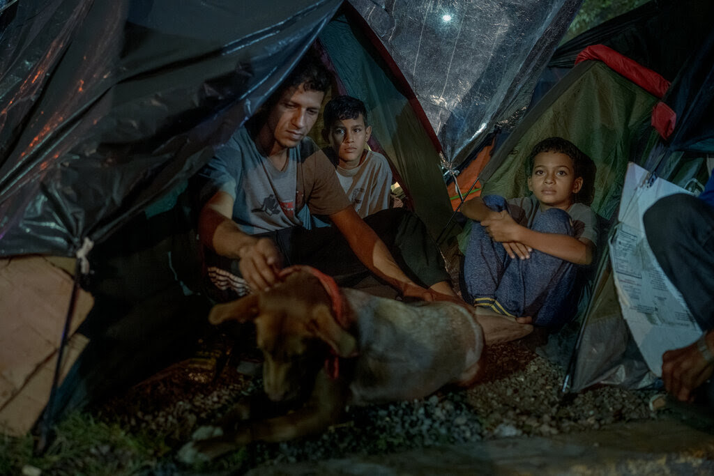 Henry Aguilar sits outside a tent with his sons as he pets the family’s dog, Donna.