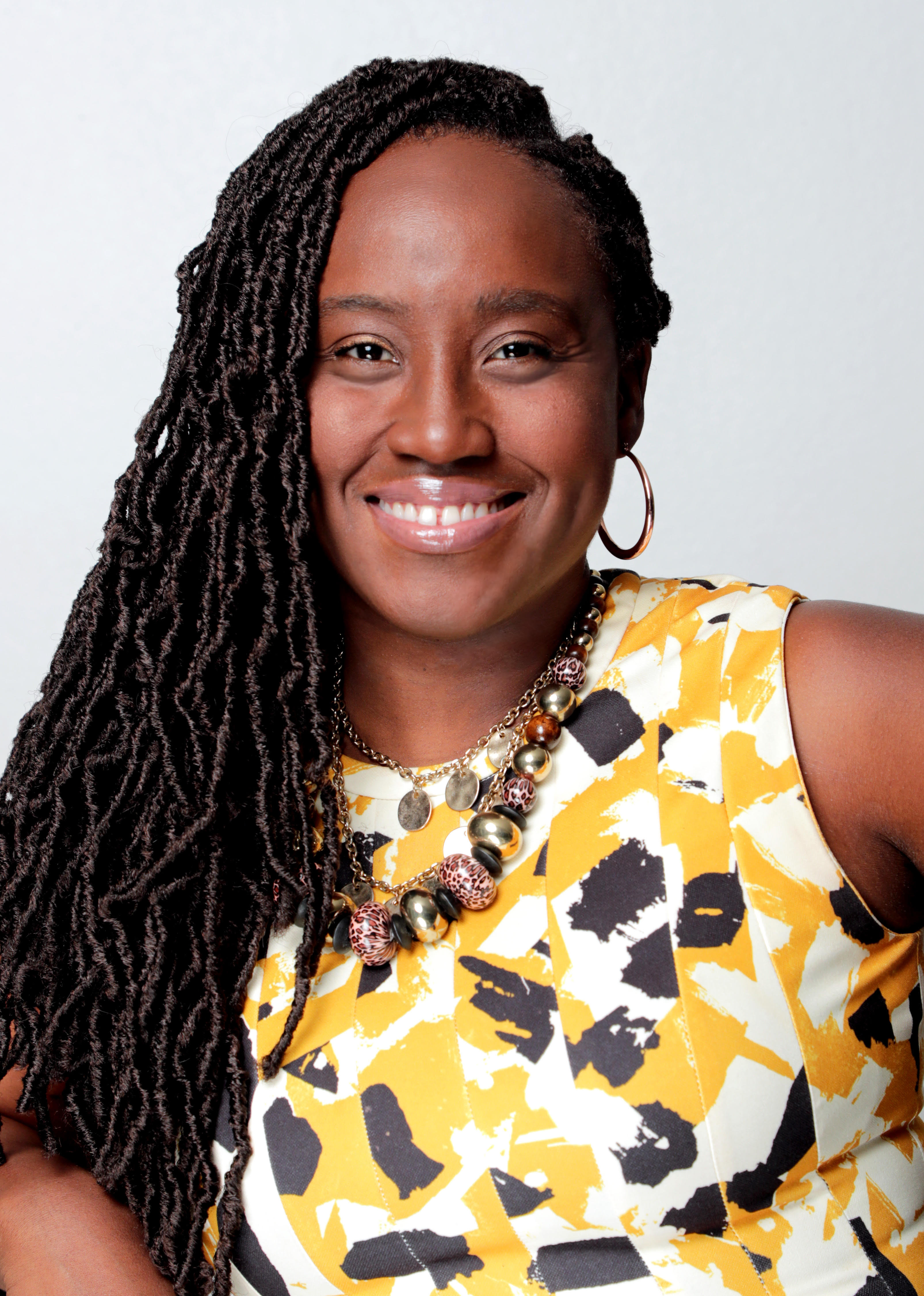A woman with a medium skin tone and long braids smile at the camera