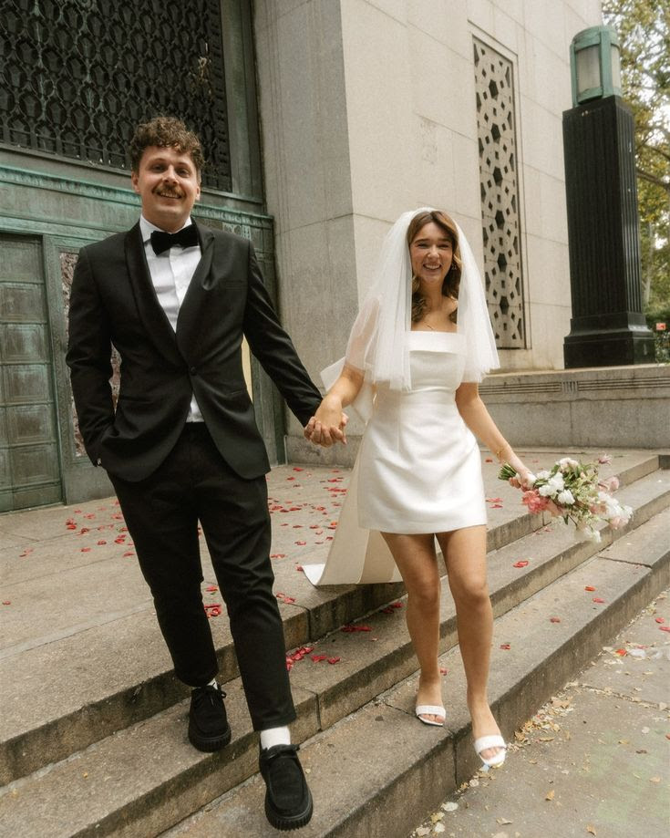 This may contain: a bride and groom are walking down the steps holding hands in front of a building