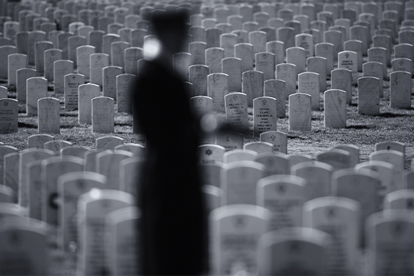 Black and white photo: figure stands in front of cemetery 