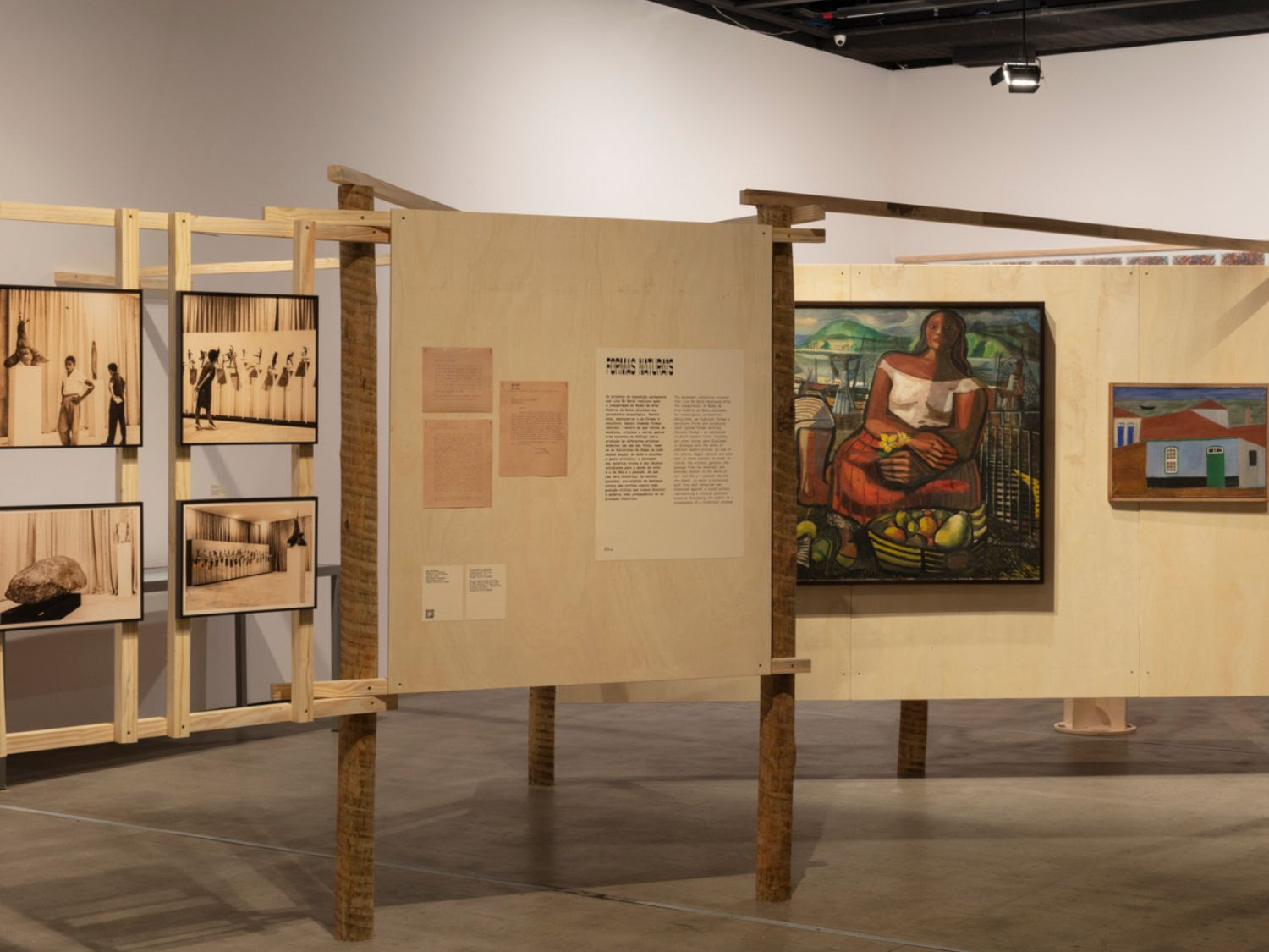 foto da exposição ensaios sobre o museu das origens. cavaletes de madeiras sustentam fotos, textos e dois quadros coloridos