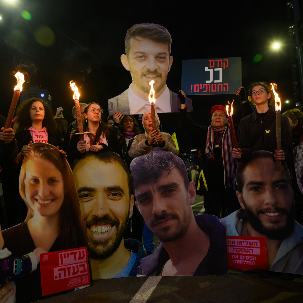 A crowd carries torch lights and large posters with the faces of Israeli hostages at night.