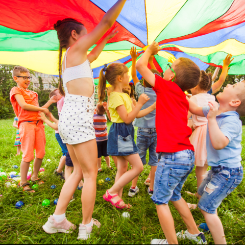 Happy young children playing with a rainbow parachute