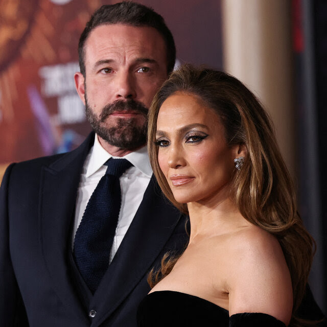 Ben Affleck and Jennifer Lopez in glamorous evening attire at a movie premiere. Mr. Affleck wears a dark suit and navy blue knit tie; Ms. Lopez is in an off-the-shoulder black gown and smoky eye makeup.