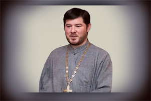 Father Kostiantyn Maksimov in a grey robe. He is wearing a large cross around his neck.