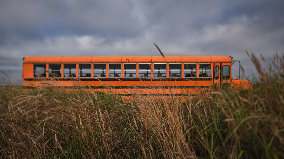 An image of a school bus driving down the road and passing tumbleweed