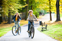 two young people ride their bikes through a green park, they are smiling