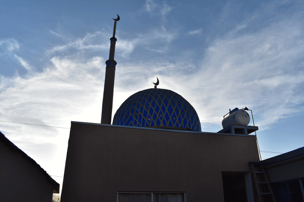 Mosque with a blue dome surrounded by slightly cloudy sky.