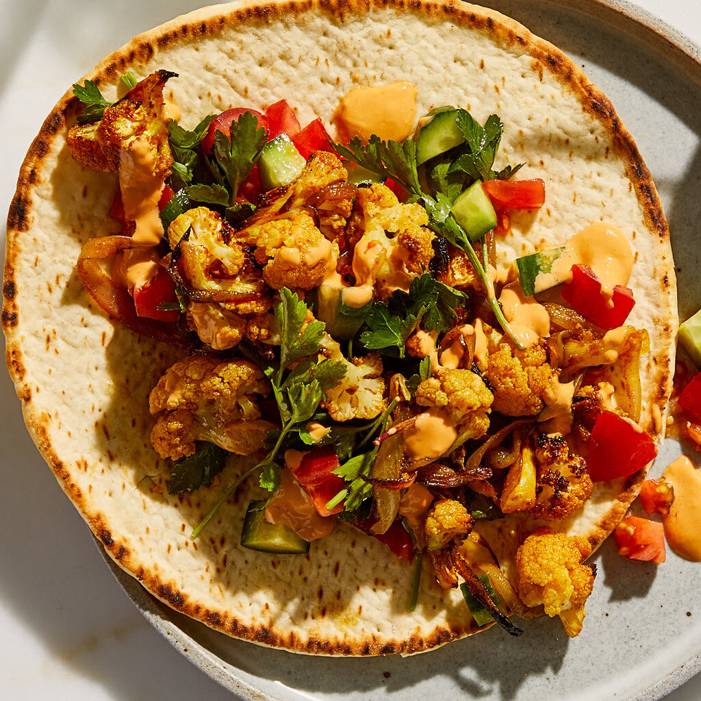 Cauliflower shawarma, topped with herbs, tomato and cucumber,  on a piece of flatbread. 