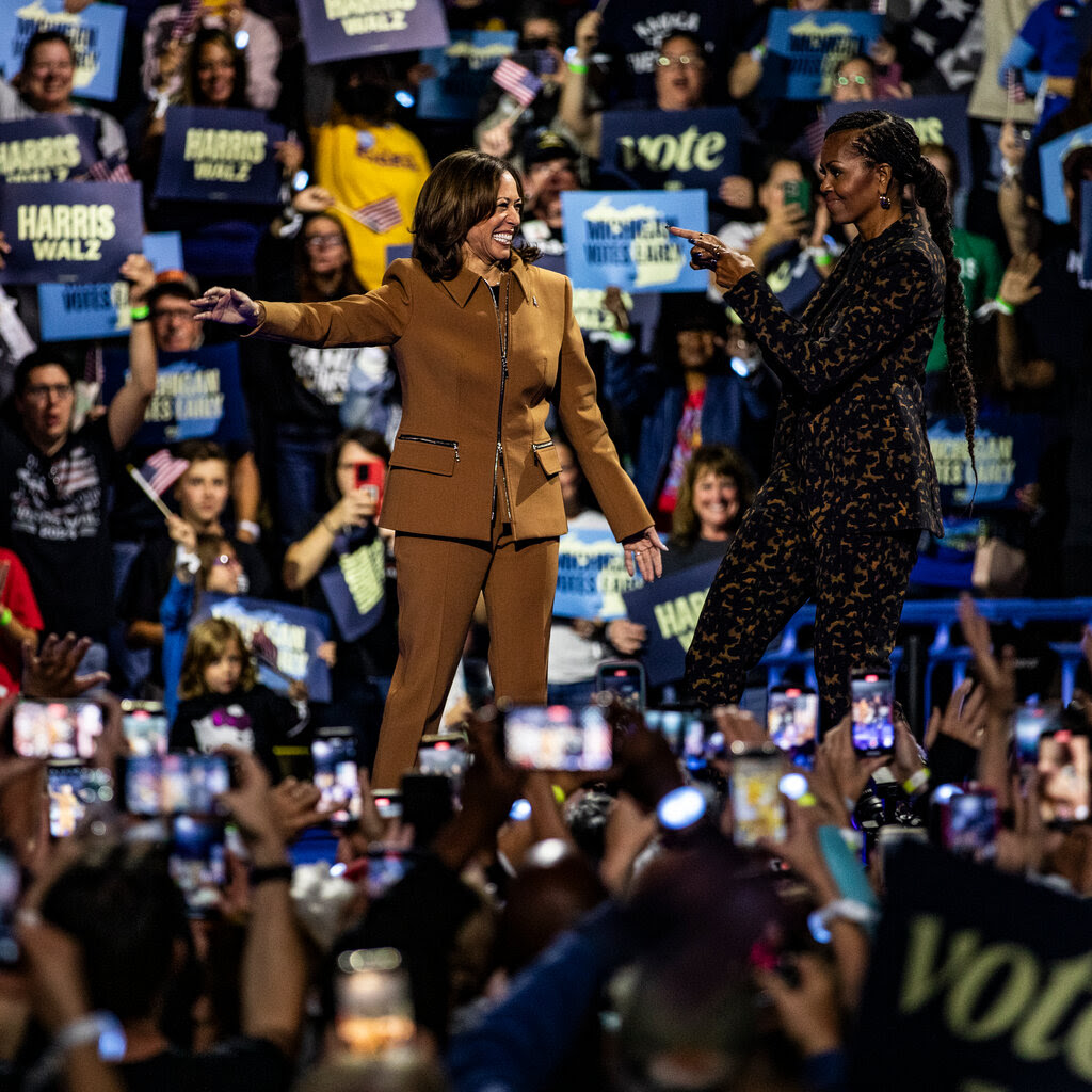 Michelle Obama points at Kamala Harris on a stage in front of a crowd.