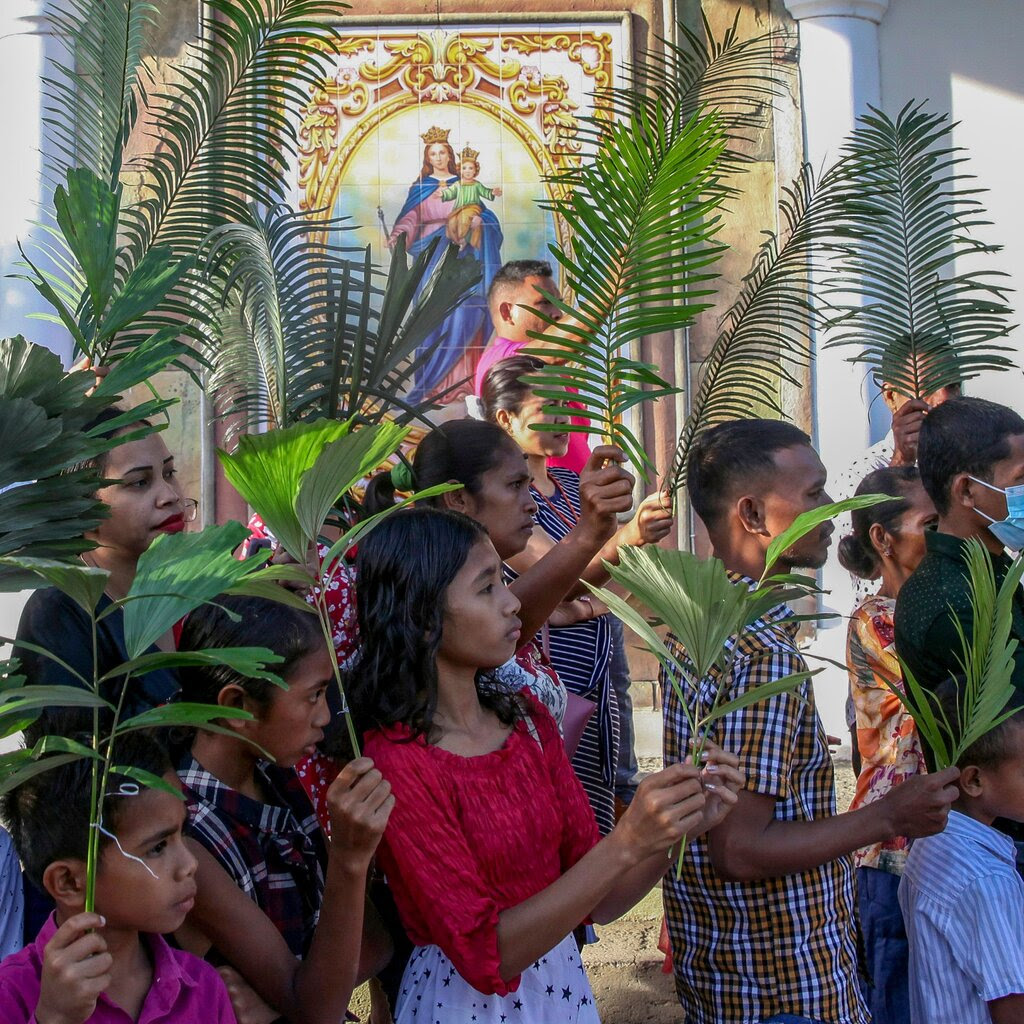 A line of people in front of a church. Each person is holding a palm frond.