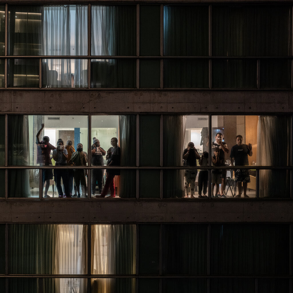 People standing on different floors inside a building and looking out the windows.