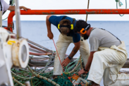 Matt Loughlin and David Axelsson from the Dyrsten crew secure a small instrument to a net aboard a fishing vessel