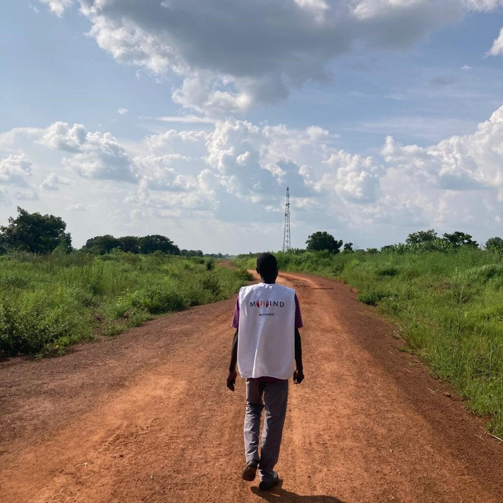 A man strolls along a dirt road in a rural setting.