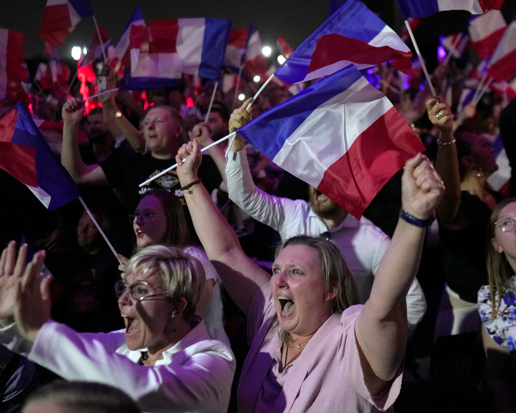 A crowd of people shout and wave French flags.