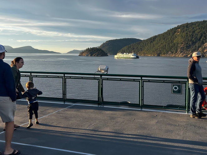 View of a ferry sailing in the waters off San Juan Islands as seen from another ferry with people on the outdoor deck in foreground