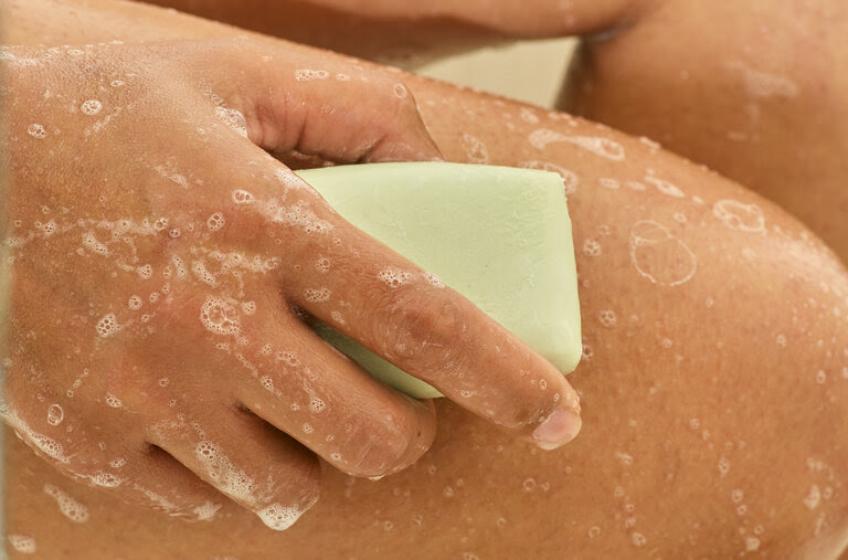 Closeup of a hand holding a bar of soap and lathering it onto their leg.