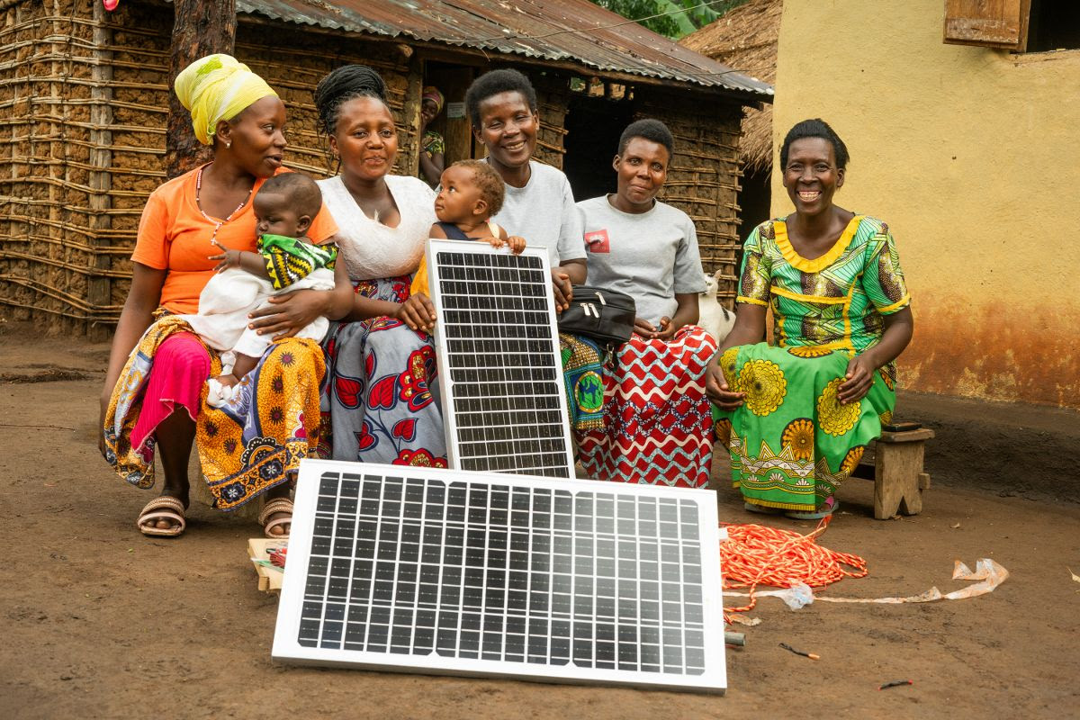 Image depicts a group of women and children from the local community in Uganda holding solar panels