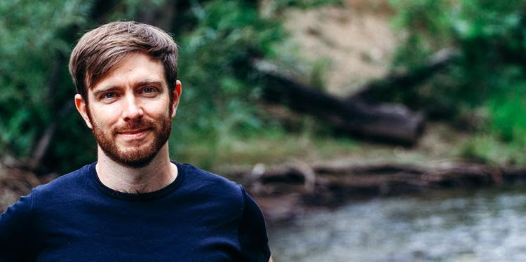 Flavio Lehner standing outside in front of water and green trees