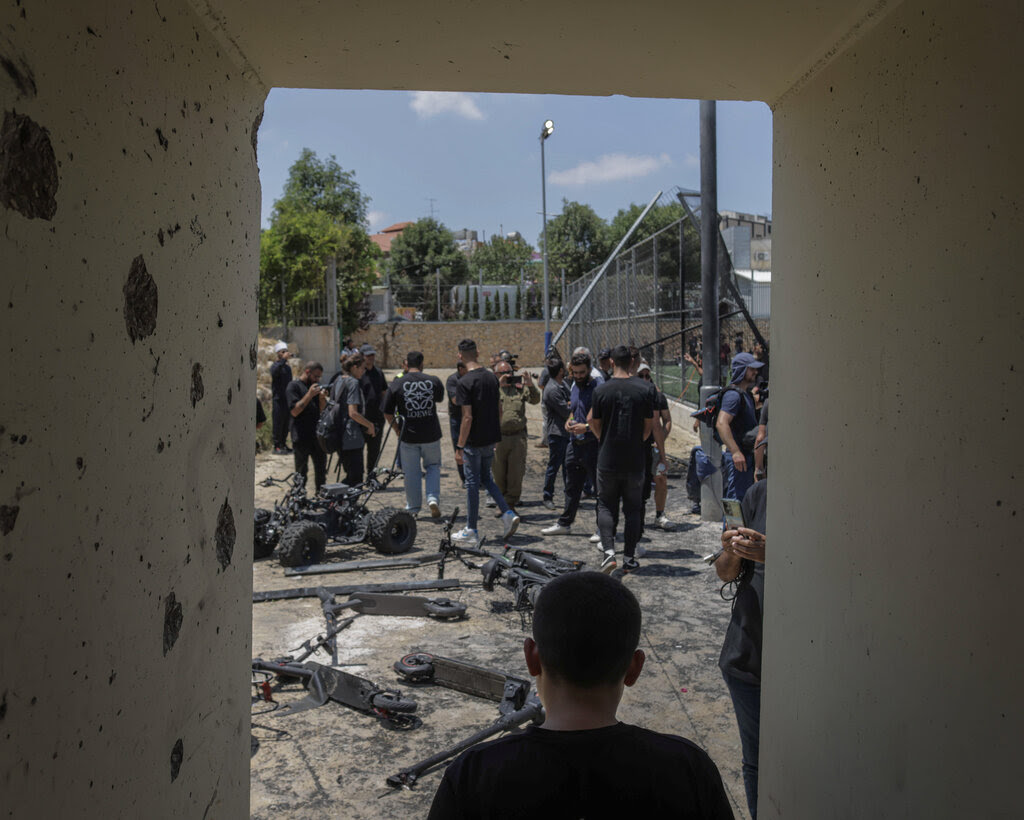 A child looks on from a concrete bomb shelter at a crowd of people and charred scooters next to a soccer field.