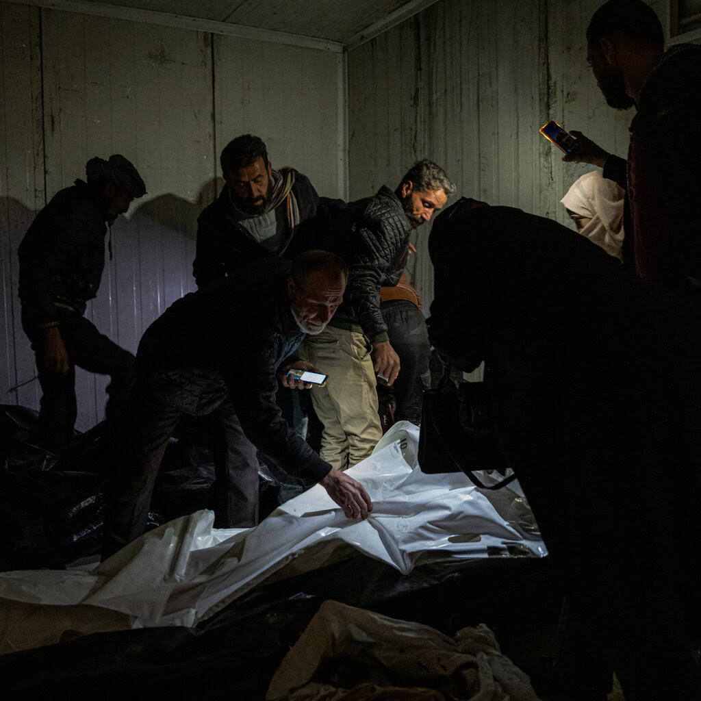 People in a dark room, examining white plastic body bags with cellphone torches.