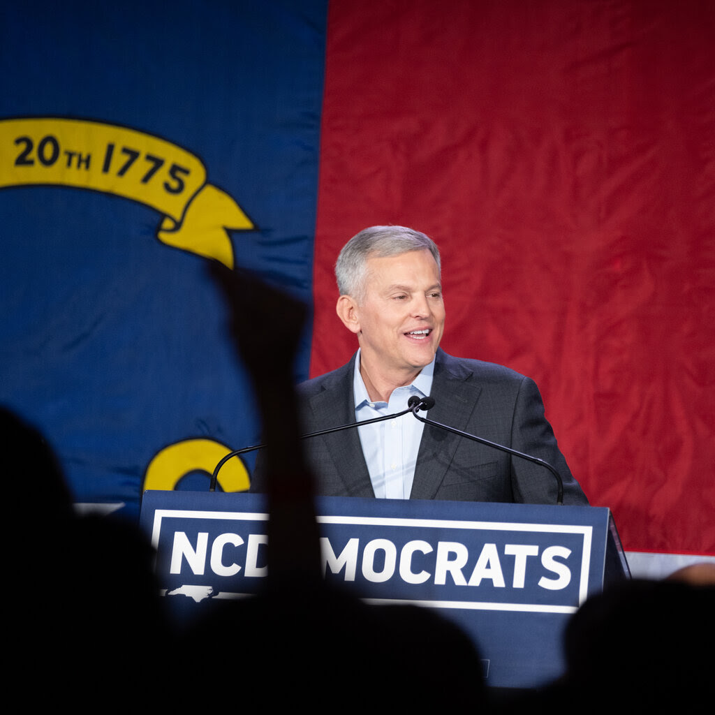 A man with gray hair and a suit gives a speech at a lectern. 