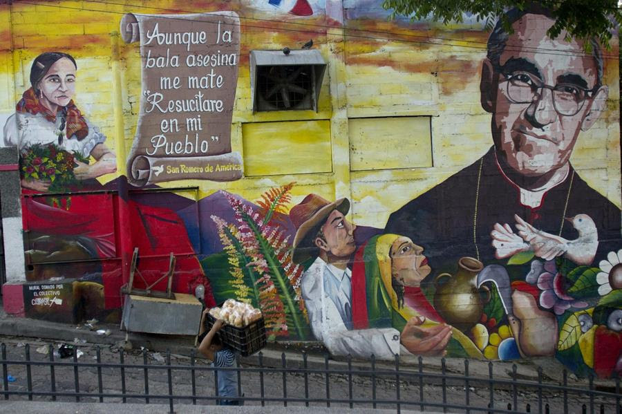 A man walks past an outdoor mural showing several figures, including one in a black priest's robe.