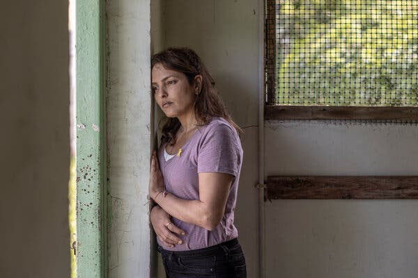 Una mujer apoyada contra una pared. Detrás de ella hay una ventana.