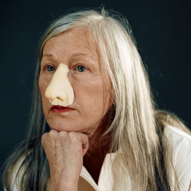 Sherman, wearing a fake nose, poses with one hand under her chin.