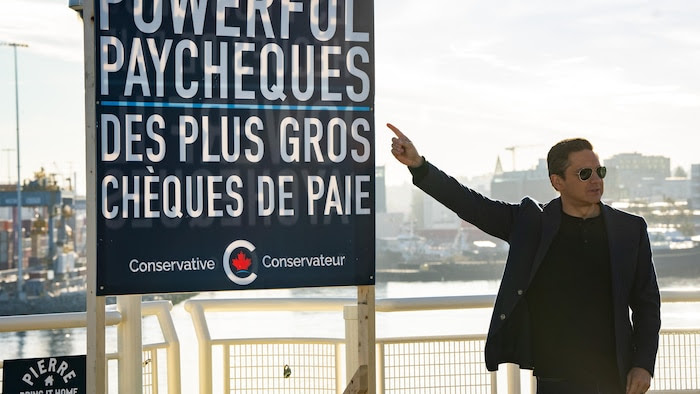 Pierre Poilievre points to a sign that says: “Bigger paychecks.”