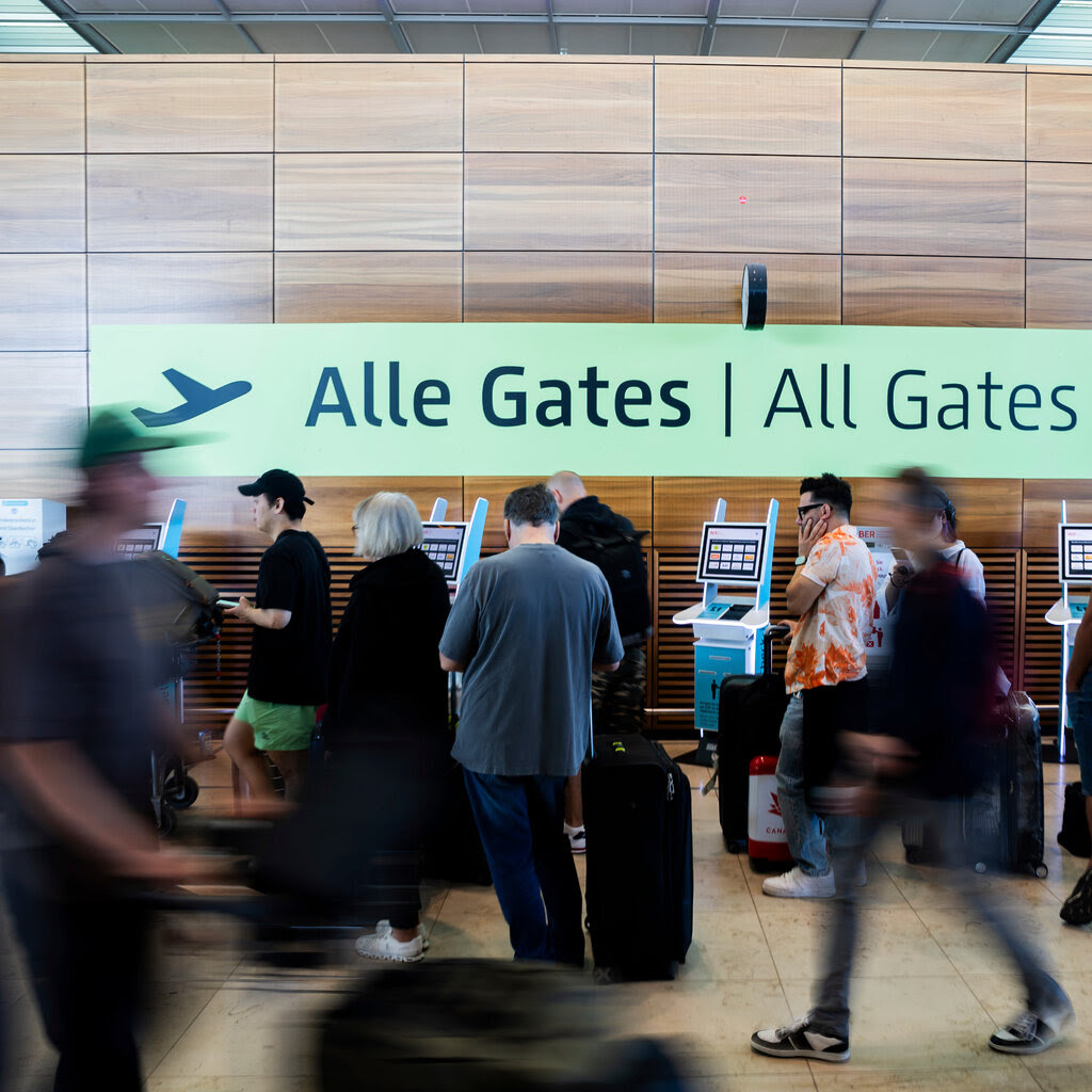 At an airport, passengers transiting through a terminal are a blur of activity. Behind them is a sign with the words “All Gates.”