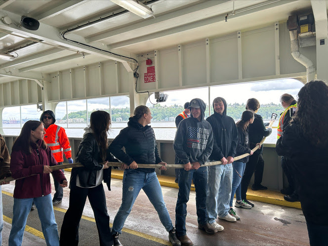 Several people lined up on the car deck of a ferry holding a firehose that extends over the side of the vessel
