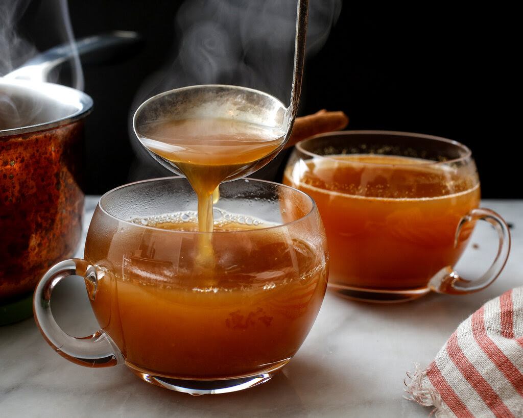 Hot apple cider pours from a ladle into a clear glass.