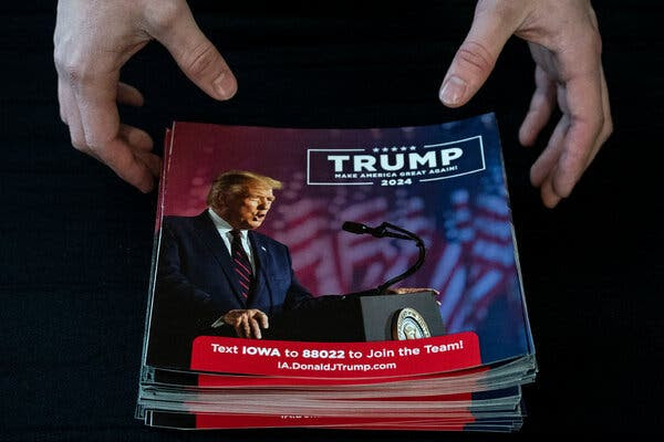 A stack of Trump fliers on a table. A pair of hands at the top is reaching for the pile, as if to straighten them out.