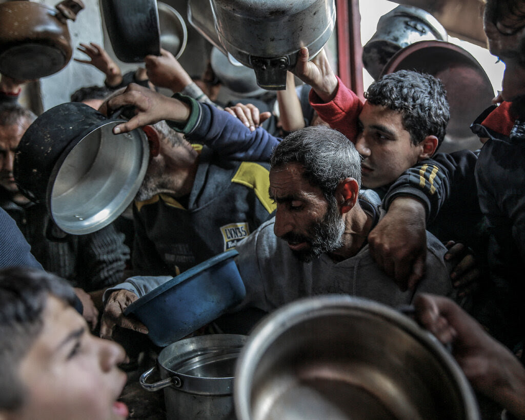 People holding pots and pans at a food distribution area. 