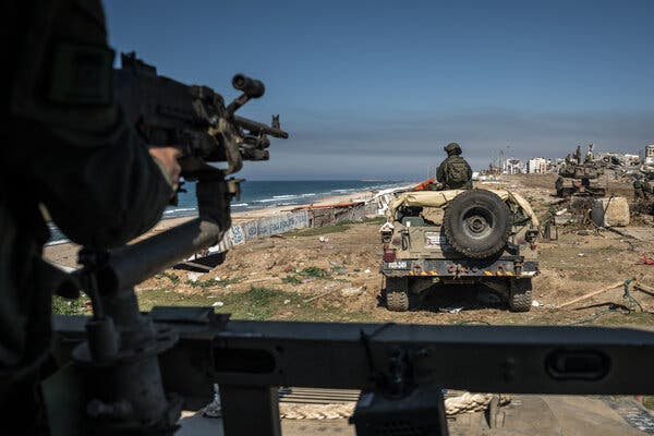 Israeli troops in Gaza during an escorted tour by the Israeli military in February. In the foreground is a soldier holding a gun, with an Israeli vehicle in front of him. 