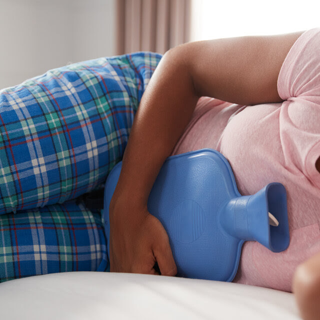 A girl wearing pajamas holds a hot water bottle onto her stomach. 