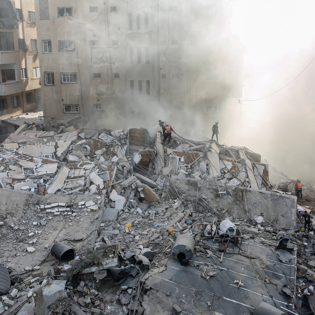 Palestinian citizens inspect a destroyed building. A cloud of dust floats above. 