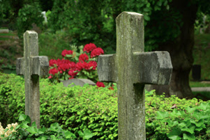 Two cross-shapped headstones are surrounded by greenery.