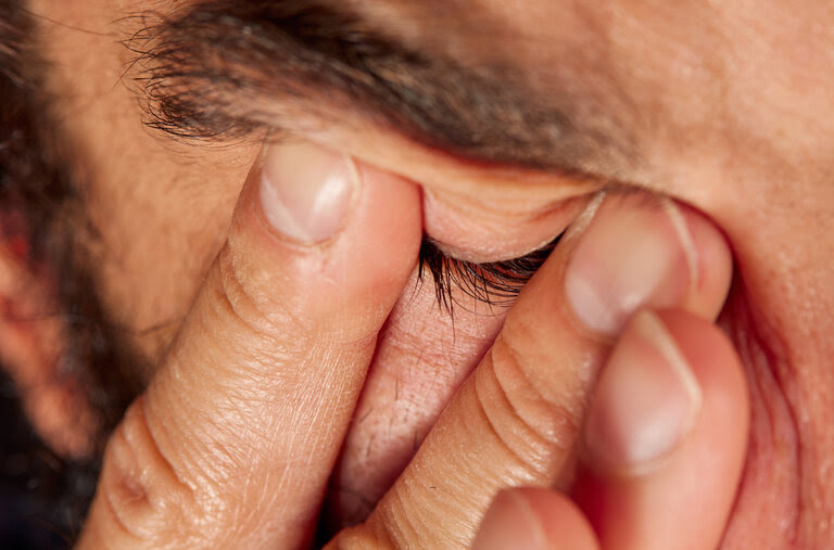 A photograph of a man rubbing his eyes.